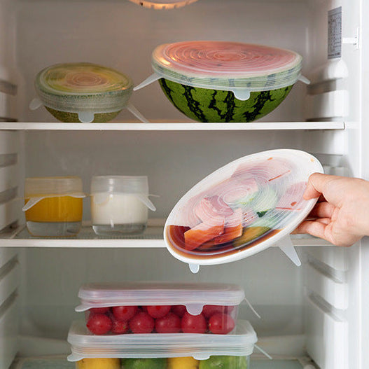 Hand opening a refrigerator door with a container of food inside.