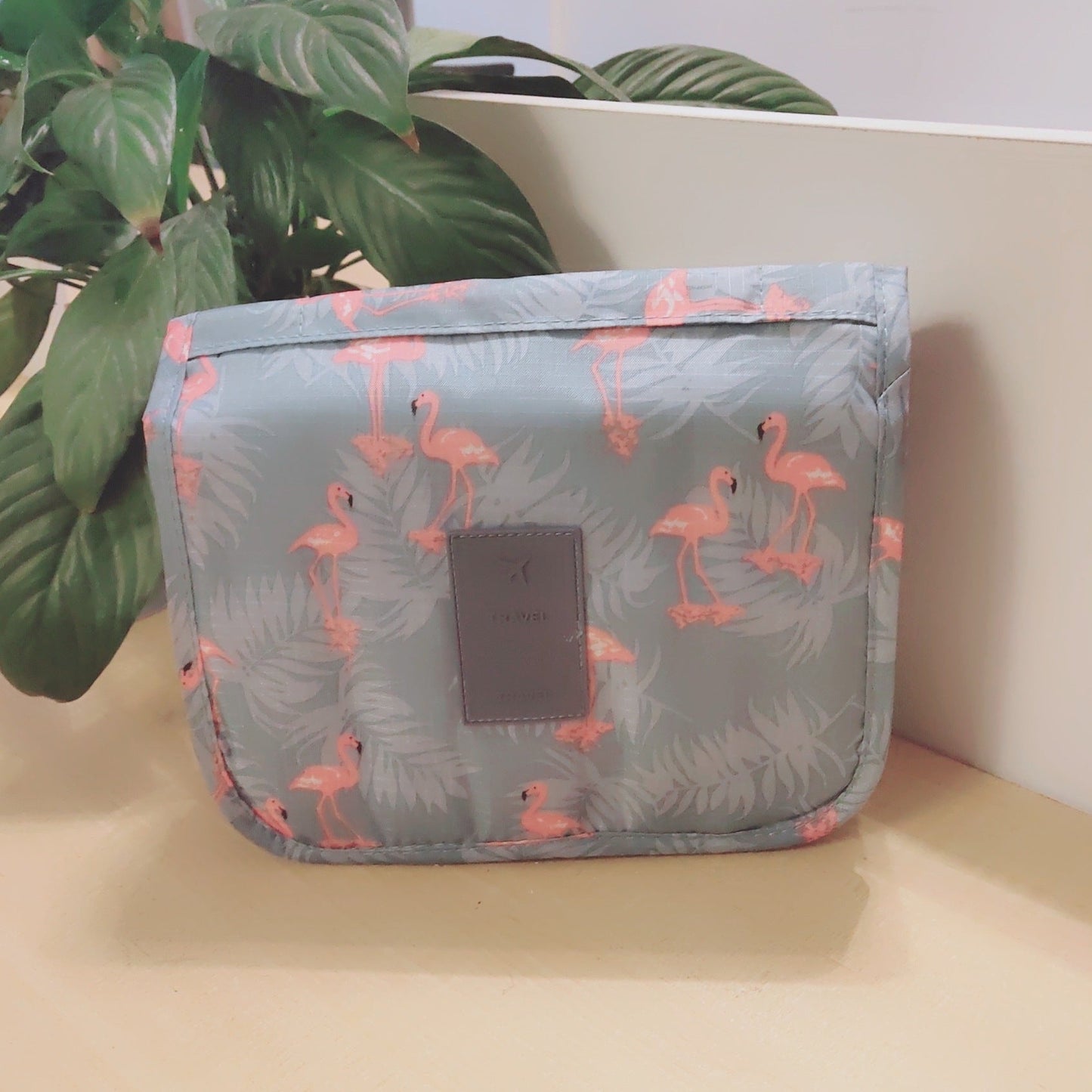 Gray pouch with flamingo pattern on a light surface with a plant in the background