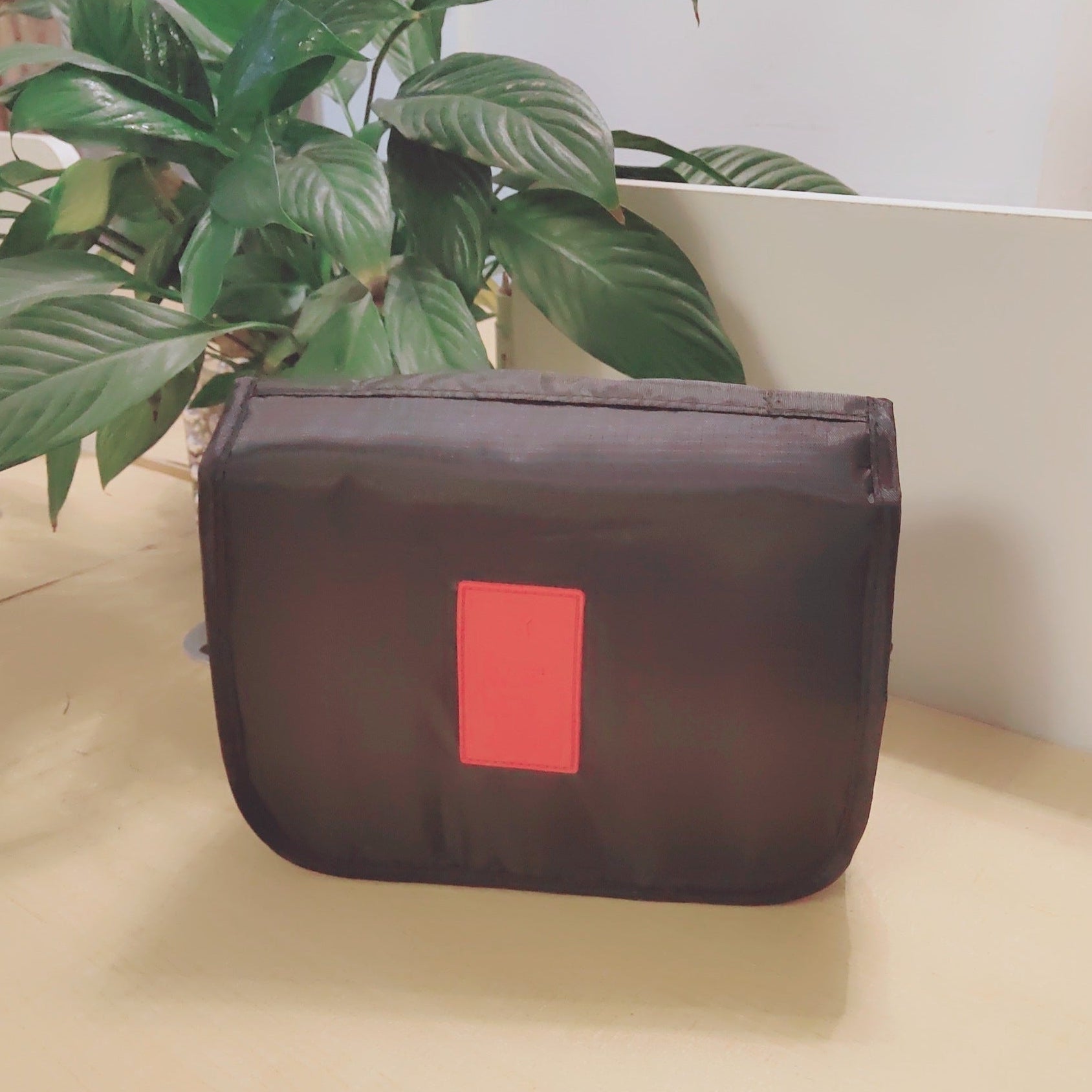 Black pouch with a red label on a beige surface with plants in the background