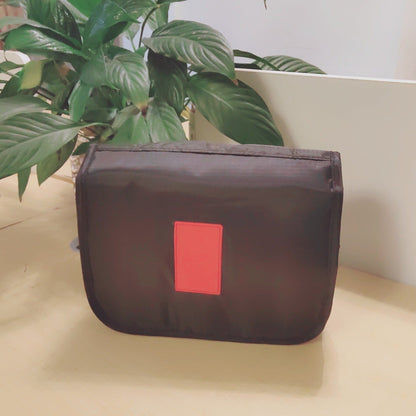 Black pouch with a red label on a beige surface with plants in the background