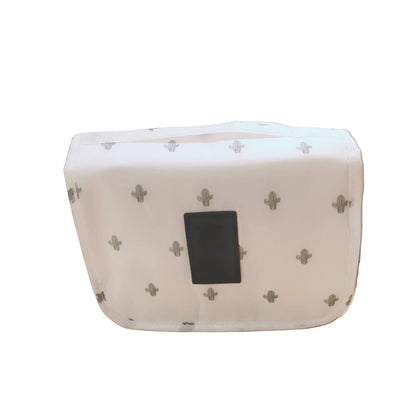 White pouch with black square on a beige surface with green plants in the background