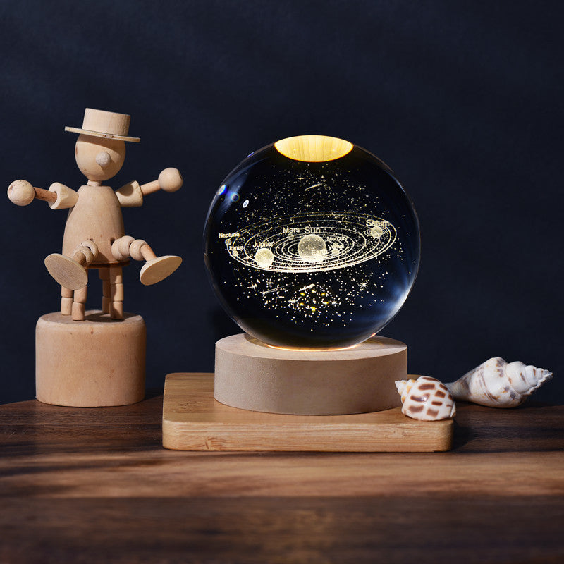 3D Galaxy Ball Night Light on a wooden stand, next to a wooden figure and seashells.