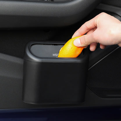 Hand placing a lemon into a black car trash can mounted on a car's interior door panel.