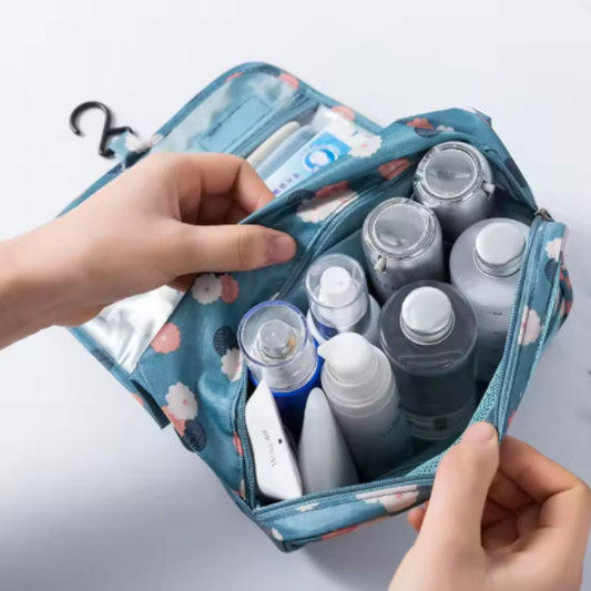 Hand holding a floral-patterned toiletry bag with various bottles inside on a light gray background