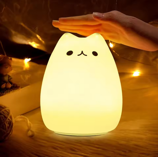 Cute cat-shaped night light with a hand holding it, surrounded by warm lighting.